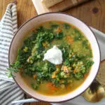 Pea soup in a pink ceramic bowl with kale and sausage