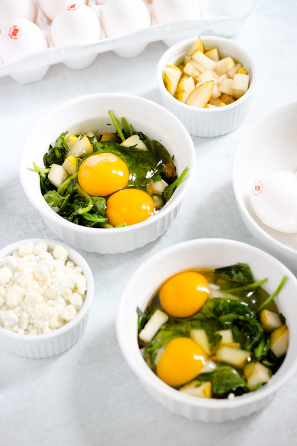 eggs cracked in ramekins with greens and ingredients