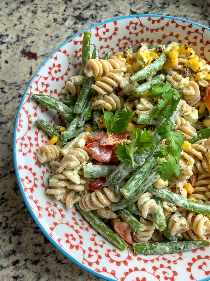 rotnini with green beans, corn, and pepper, and herbs tossed in a creamy dressing served in a blue and white bowl photographed from above
