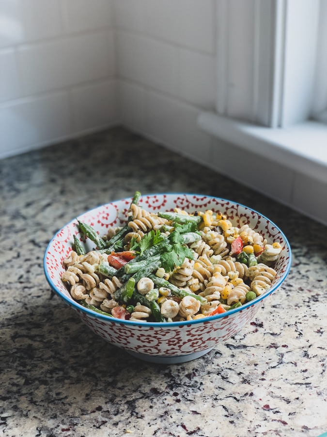 blue and white bowl of pasta salad from the side with creamy rotini pasta salad topped with fresh herbs in a kitchen with granite counters and a white backsplash