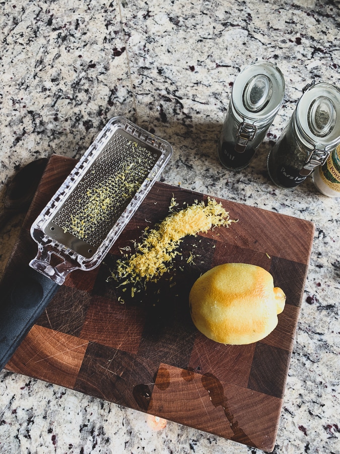 A lemon partially zested on a wooden cutting board