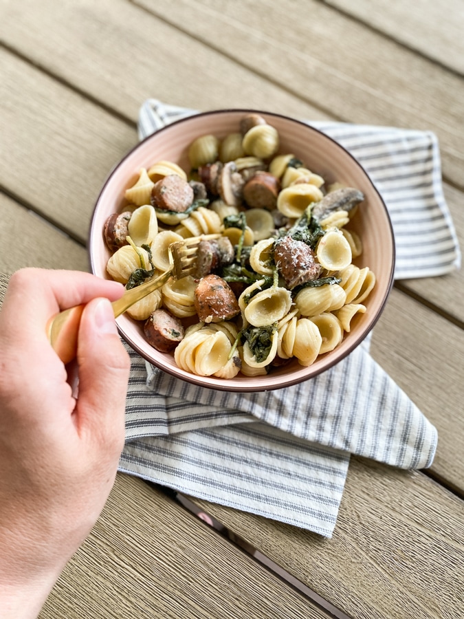 hand eating sausage pasta