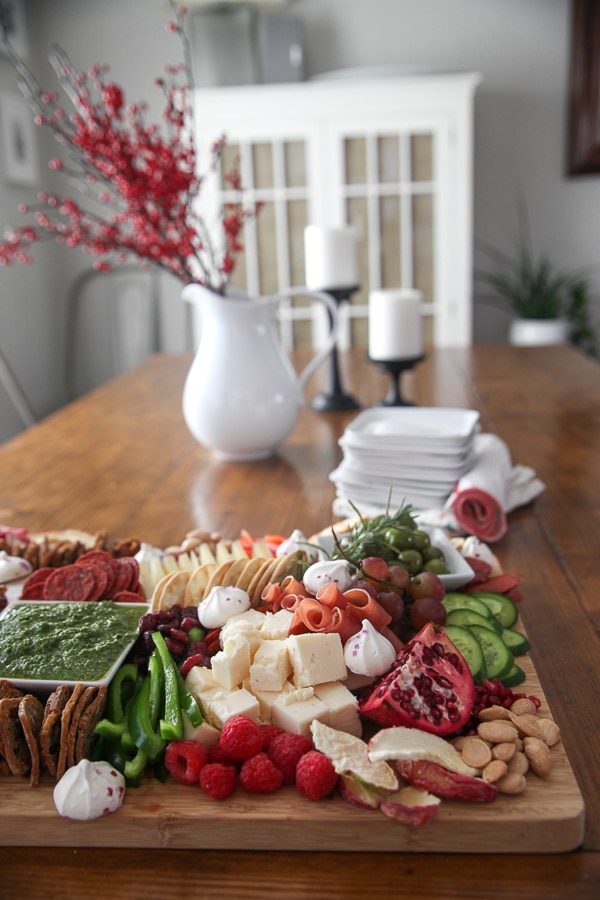 charcuterie board on a table with red berries in a pitcher and a stack of plates