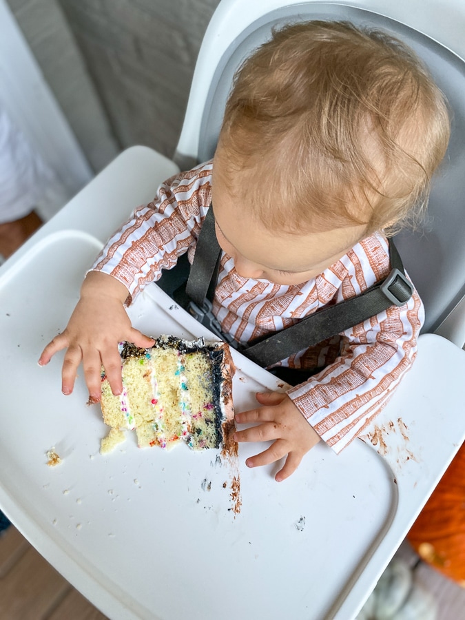 baby in high chair eating slice of birthday cake