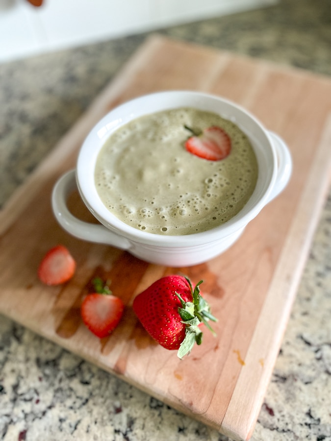 Strawberry Peach Smoothie in white bowl on wood cutting board with strawberries