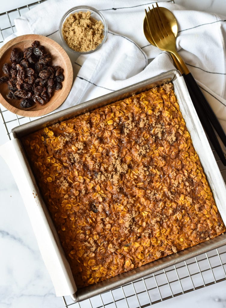 healthy baked oatmeal with pumpkin in a square pan with brown sugar and raisins on the side