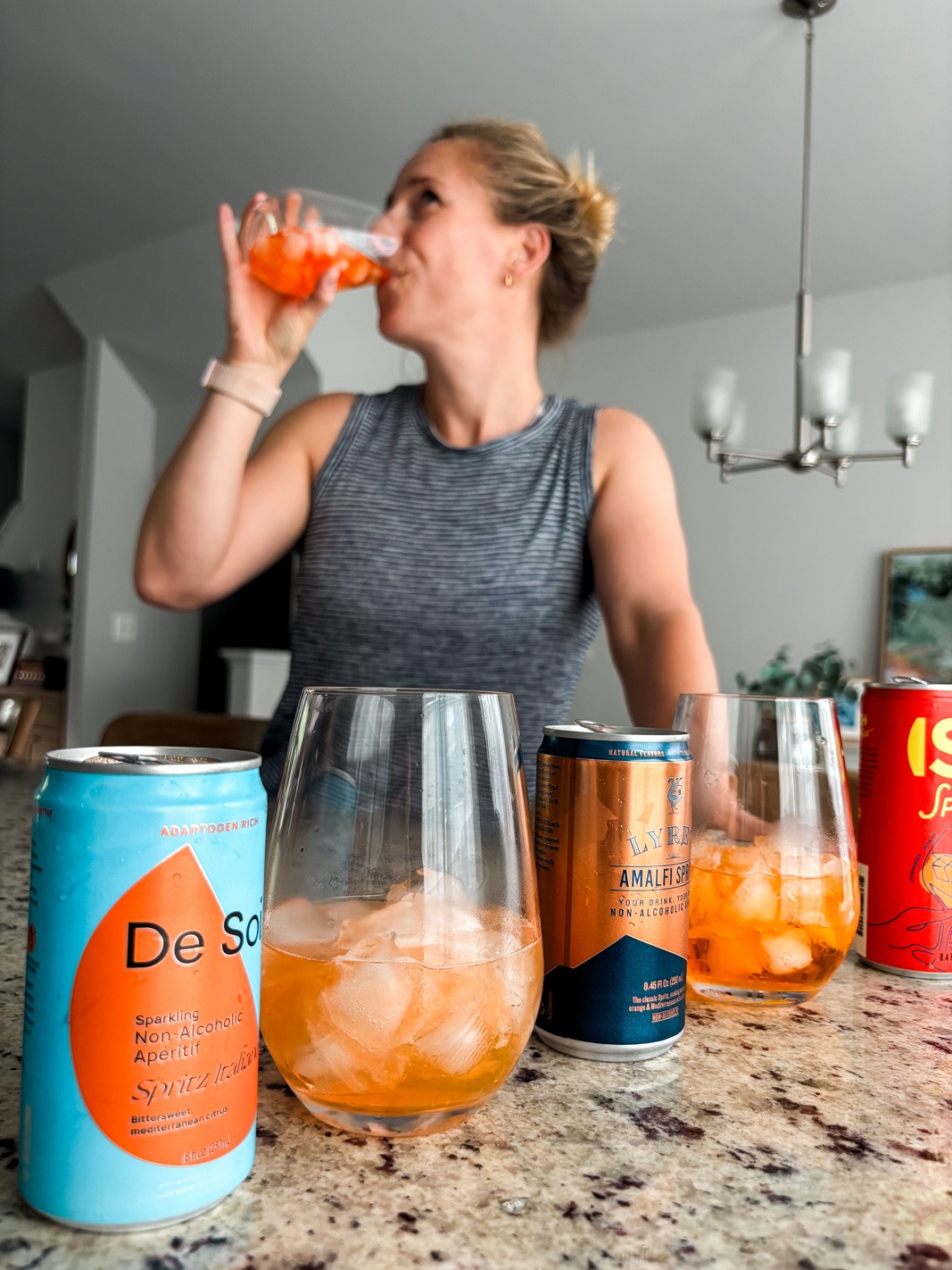 Kath drinking a nonalcoholic aperol spritz in the background with cans in the foreground
